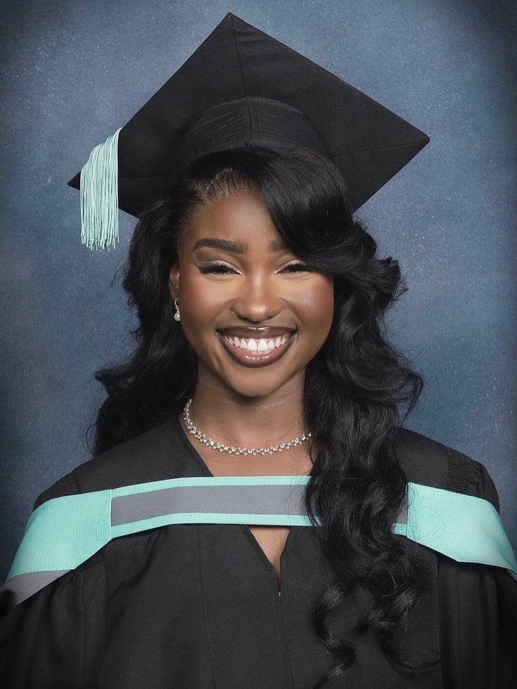 Woman with wavy black hair wearing a graduation cap and gown smiling.