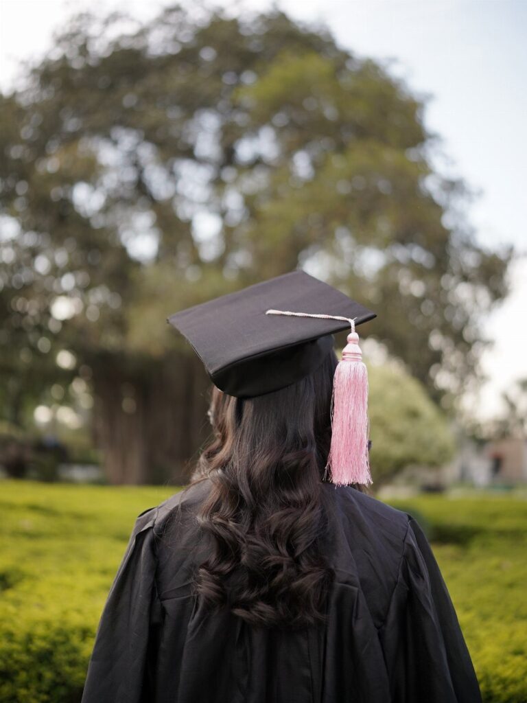 Graduate from behind wearing a black cap and gown with a pink tassel.