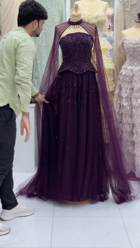 Purple sparkling prom gown with a sheer cape displayed on a mannequin.