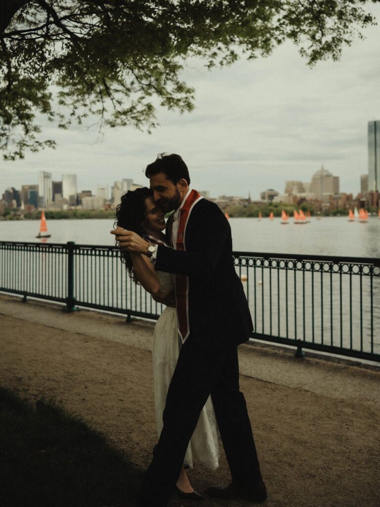 Couple dancing by the water, man wearing a graduation stole and black suit.