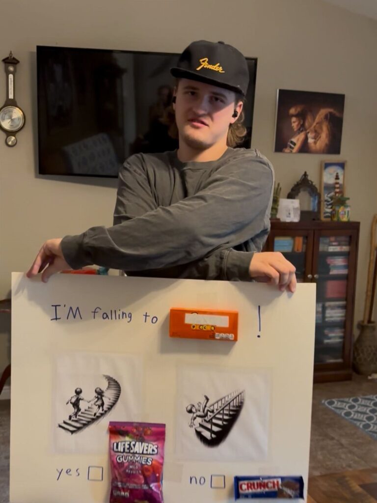Young man holding a homecoming proposal poster with candy and drawings.