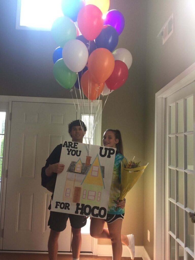 Teenage couple posing with a colorful balloon bunch and a HOCO proposal poster.