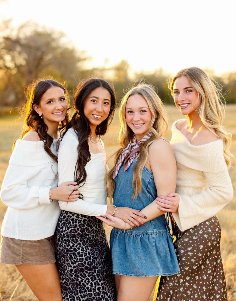 Four young women in autumn outfits posing together in a sunlit field.