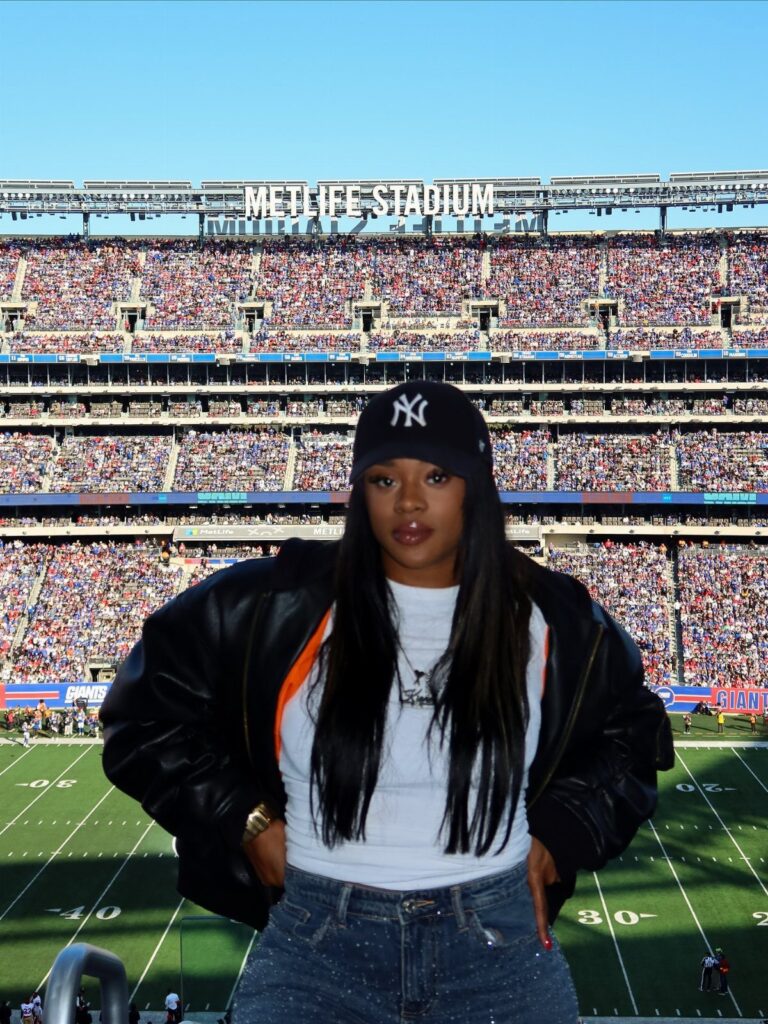 Woman wearing a leather jacket and baseball cap posing at MetLife Stadium.