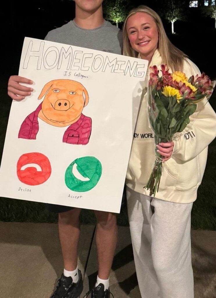 Teenage couple posing with a funny homecoming proposal poster and a flower bouquet.