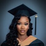 Woman with long curly black hair wearing a black graduation cap and gown.