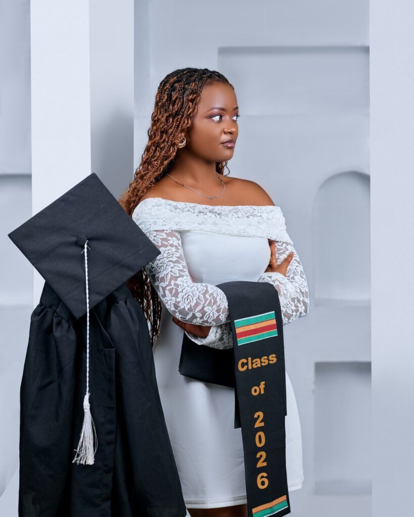 Young woman in white dress posing with graduation gown, cap, and class stole.
