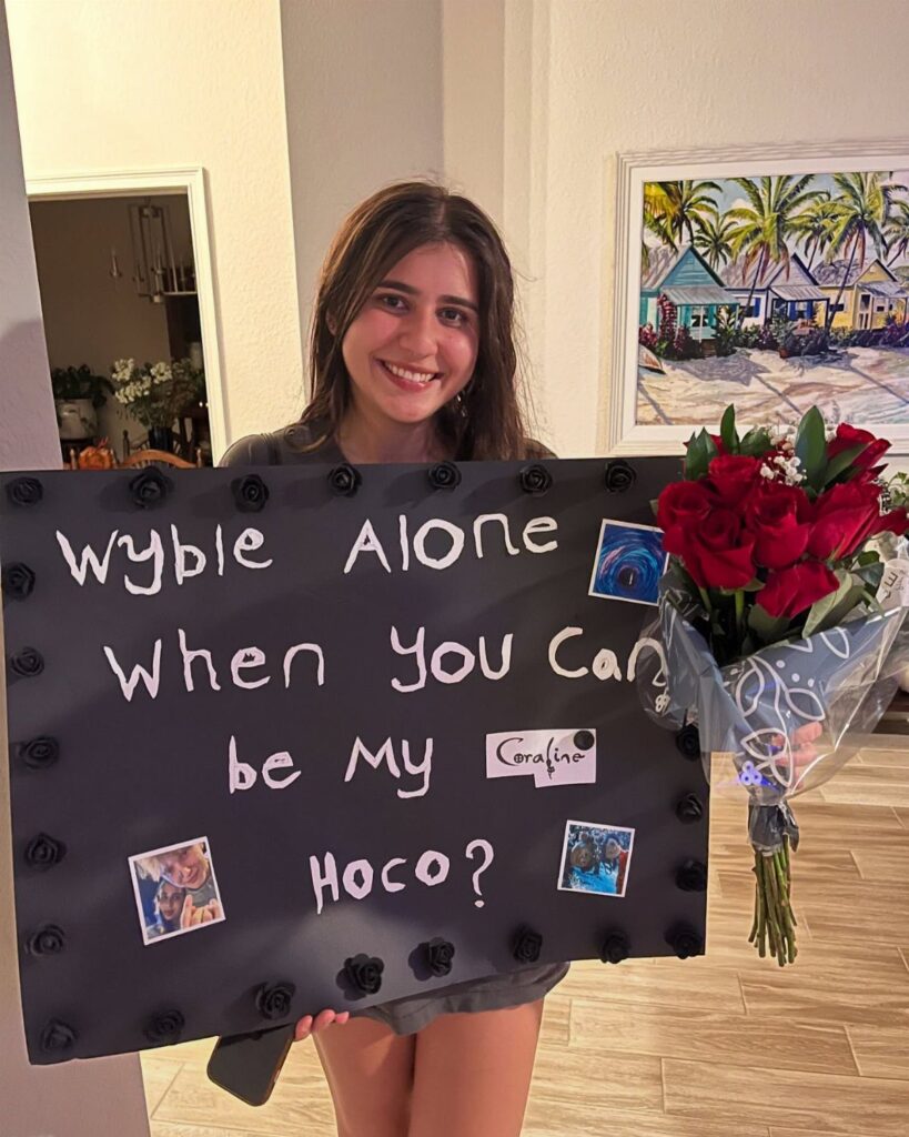 Teenage girl holding a homecoming asking poster and a bouquet of red roses.