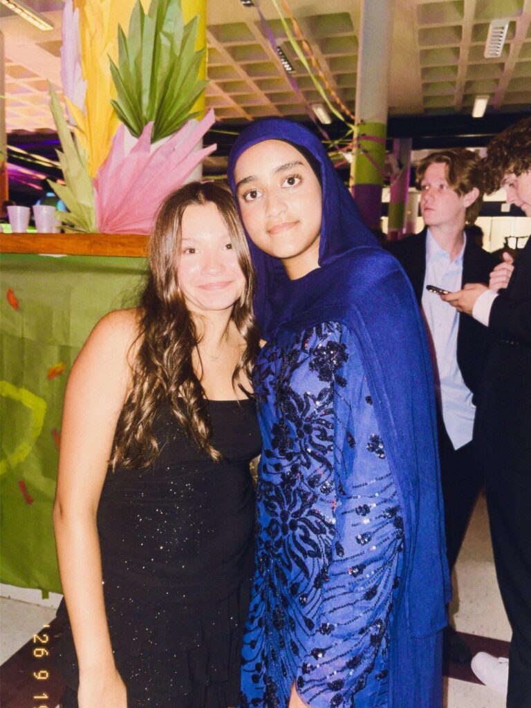 Two teenage girls posing, one in a modest blue sequined dress and hijab.