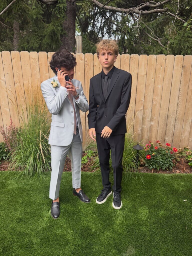 Two young men posing in grey and black suits on a green lawn.