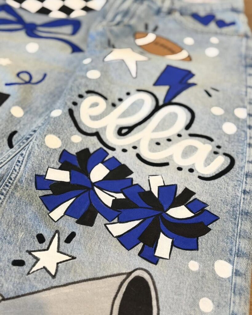 Decorated light blue jeans featuring the name Ella and cheerleader themed graphics.