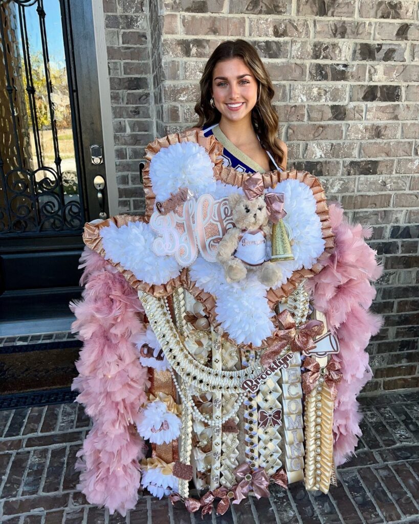 Young woman wearing a large pink and white homecoming mum with a teddy bear.