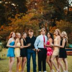 Group of teenagers in formal attire posing together on a lawn during autumn.