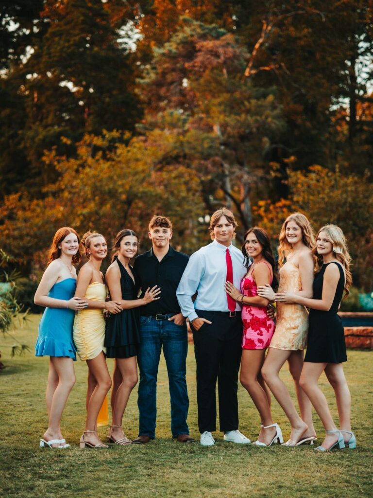 Group of teenagers in formal attire posing together on a lawn during autumn.