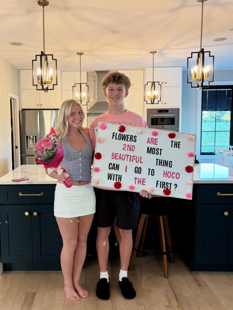 Teenage boy holding a homecoming proposal poster and girl holding pink flowers.