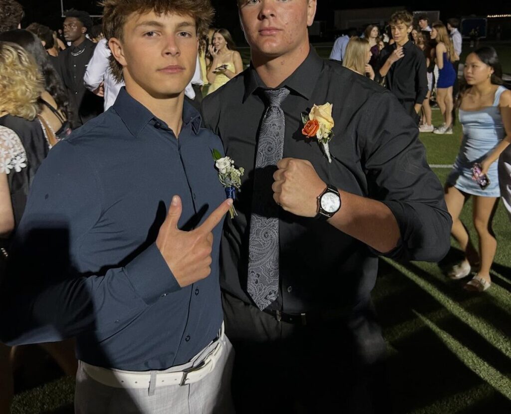 Two young men in dress shirts and trousers posing at a homecoming dance.