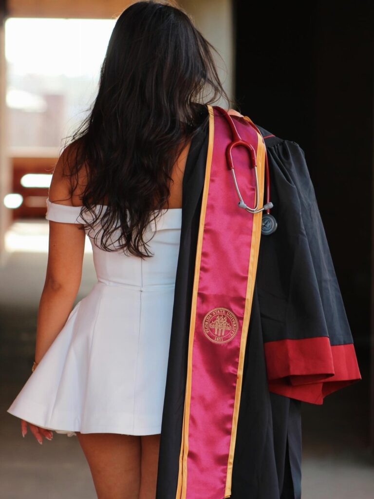 Woman in white dress carrying a graduation gown and stethoscope over her shoulder