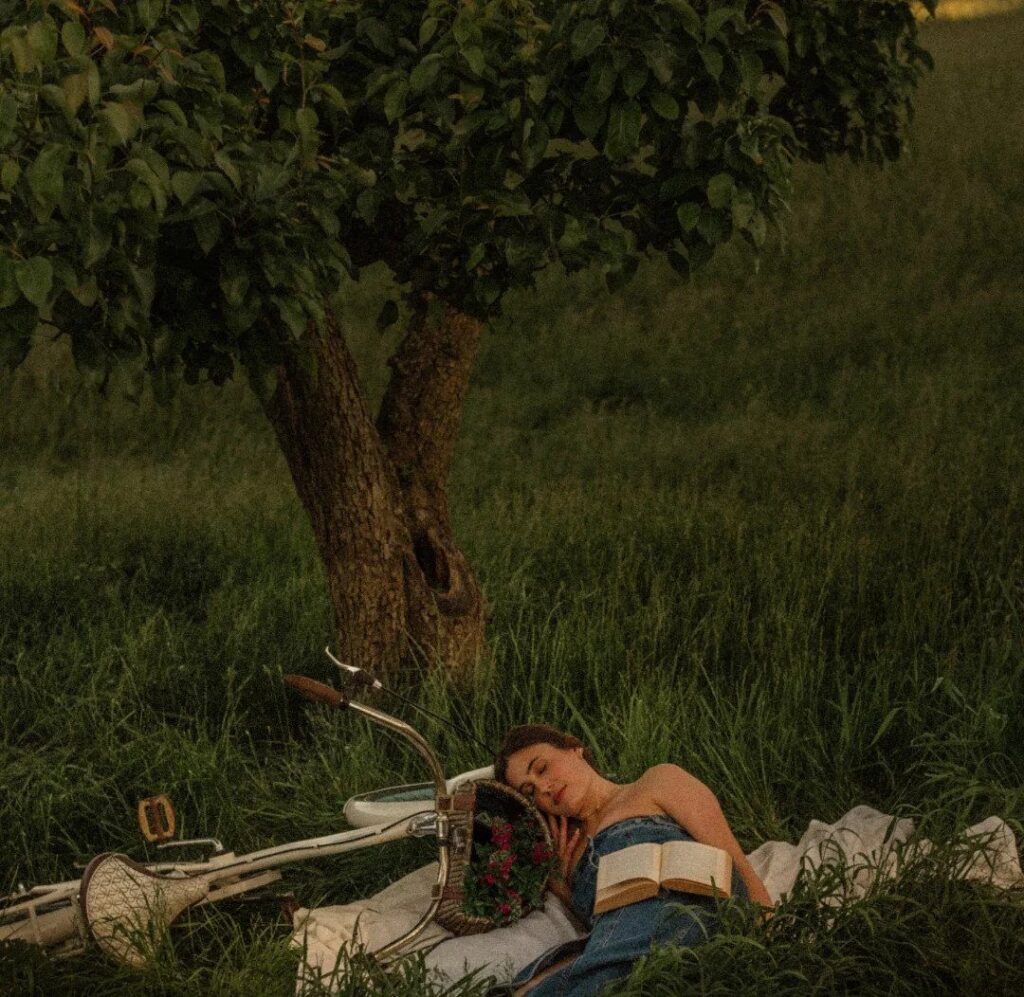 Young woman reading a book while lying on a blanket beside a vintage bicycle