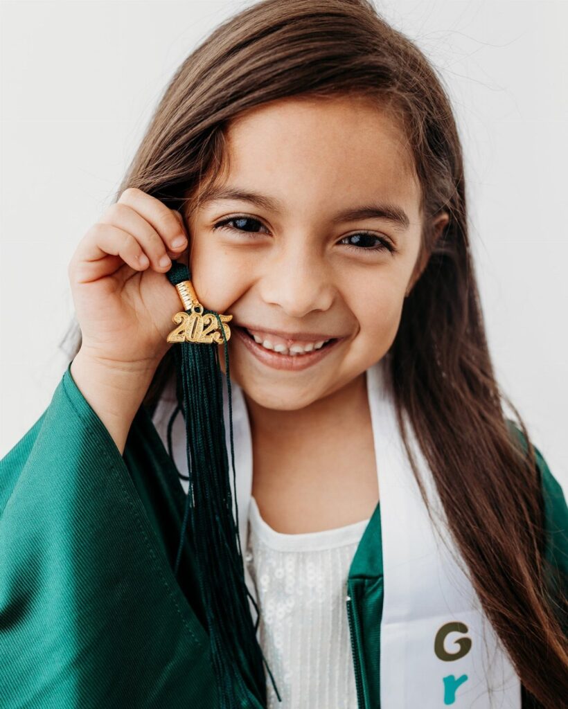 Smiling young girl in a green graduation gown holding a 2021 tassel charm.
