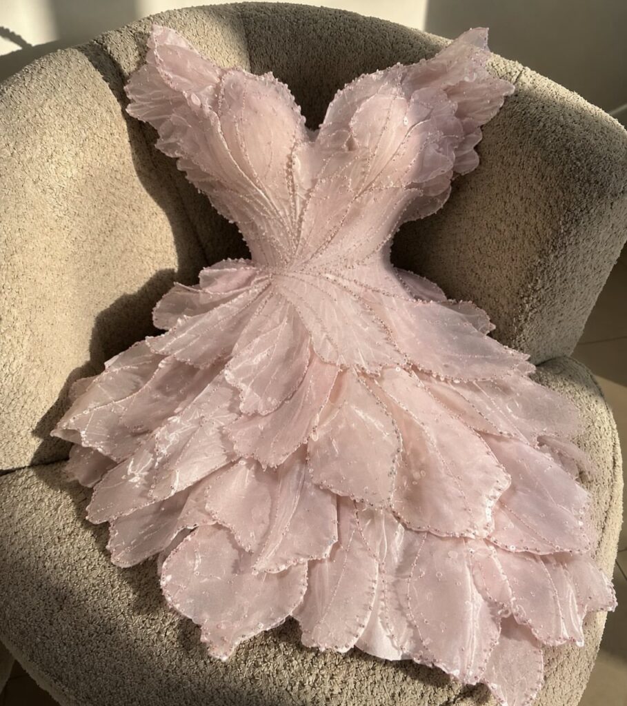 Light pink mini dress with 3D floral petal textures resting on a beige chair