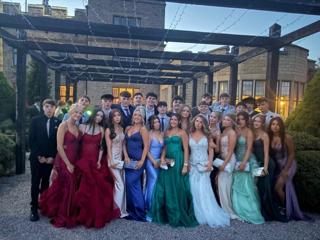Group of teenagers in formal prom dresses and suits posing under a pergola.