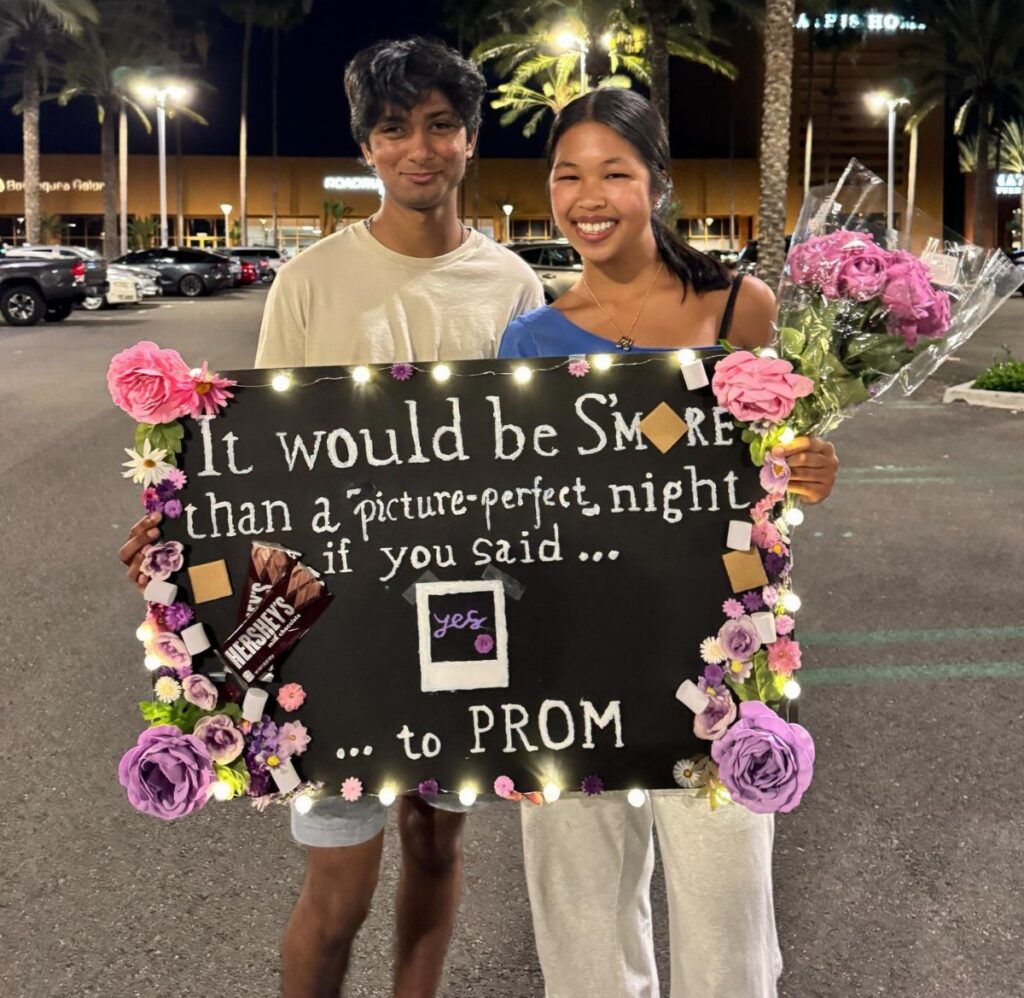 Teenage couple holding a decorated prom proposal poster and pink roses at night.