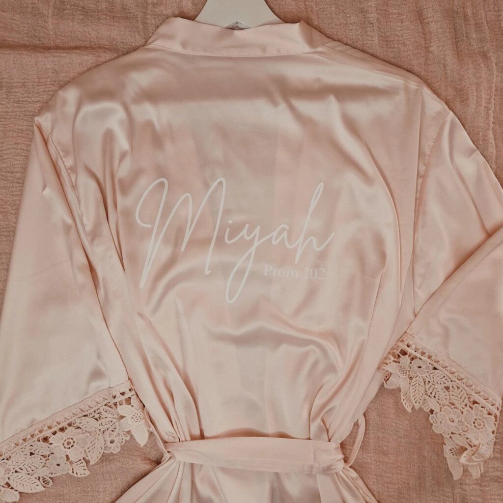 Pink satin robe with lace trim and white Prom 2021 embroidery on back