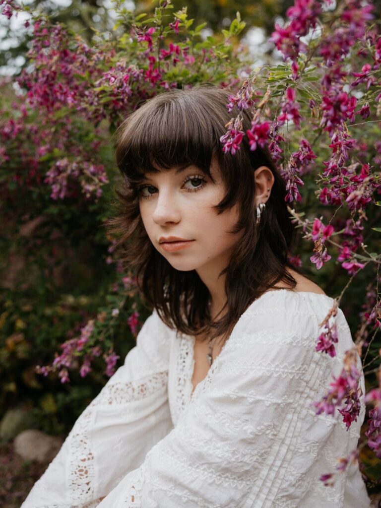 Young woman in white lace blouse posing among pink flowers in a garden