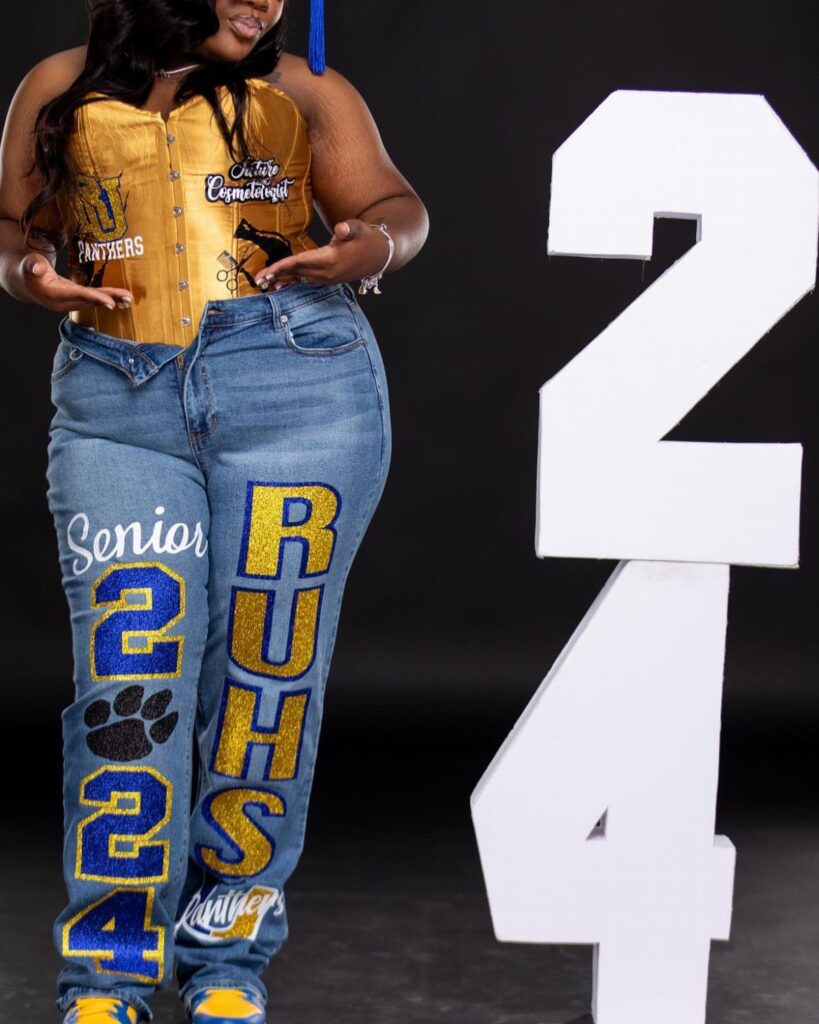 Woman in gold corset and customized senior jeans posing by large white numbers