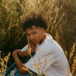 Young man in white shirt and jeans sitting in a golden grassy field