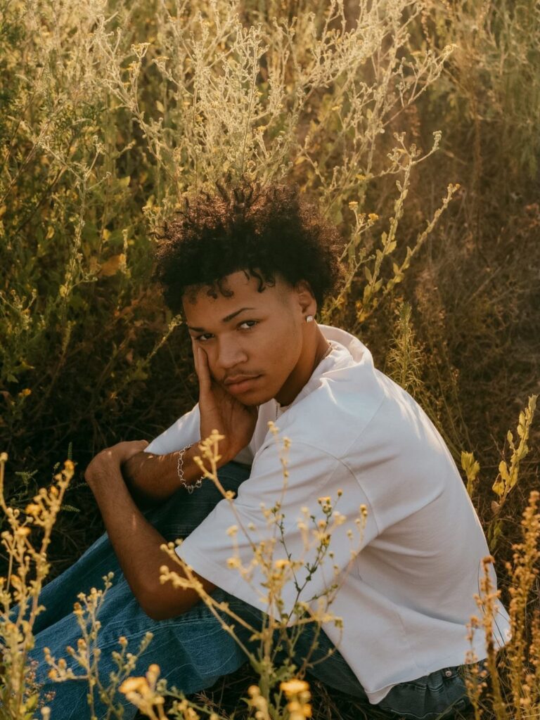 Young man in white shirt and jeans sitting in a golden grassy field