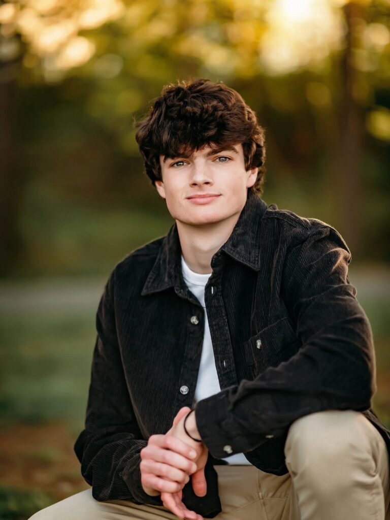 Young man in a black corduroy shirt posing for a portrait in nature.