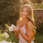 Young woman in a floral white dress posing in a sunlit rose garden