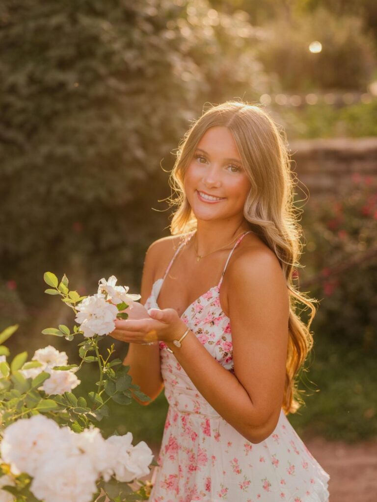 Young woman in a floral white dress posing in a sunlit rose garden