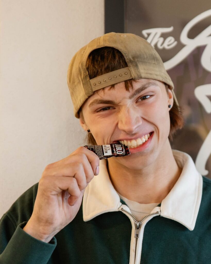 Young man in a tan cap making a funny face with a chocolate bar.