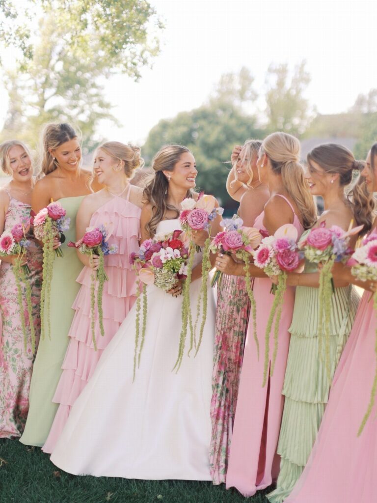 Bride in white gown surrounded by bridesmaids in pink and green party dresses