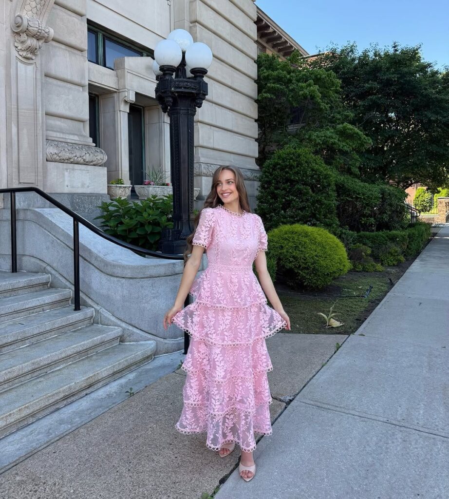 Woman wearing a tiered pink lace midi dress standing on a city sidewalk.